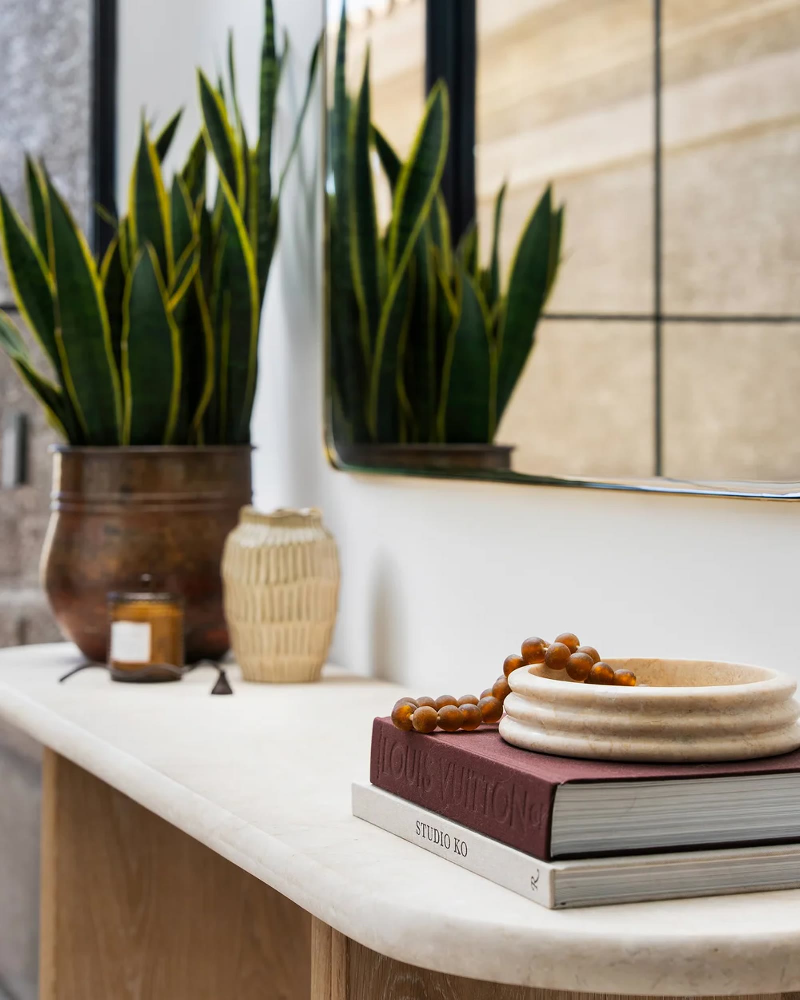 A limestone console with books, stone, and a snake plant in a copper vessel. Across the Room, Paradise Valley, Desert Dwelling.