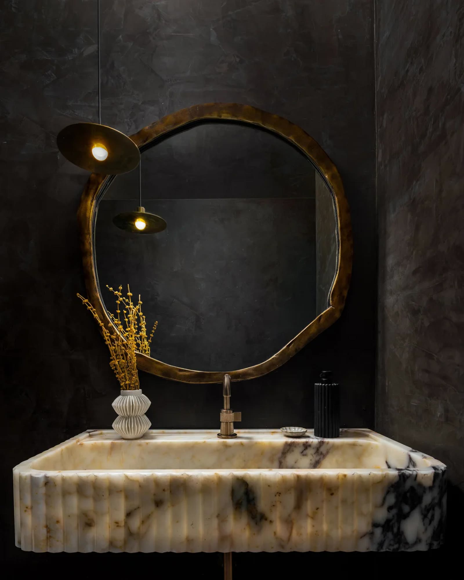 A fluted onyx sink against a dark plaster wall, with a bronze organic mirror. Across the Room, Paradise Valley, Desert Dwelling.