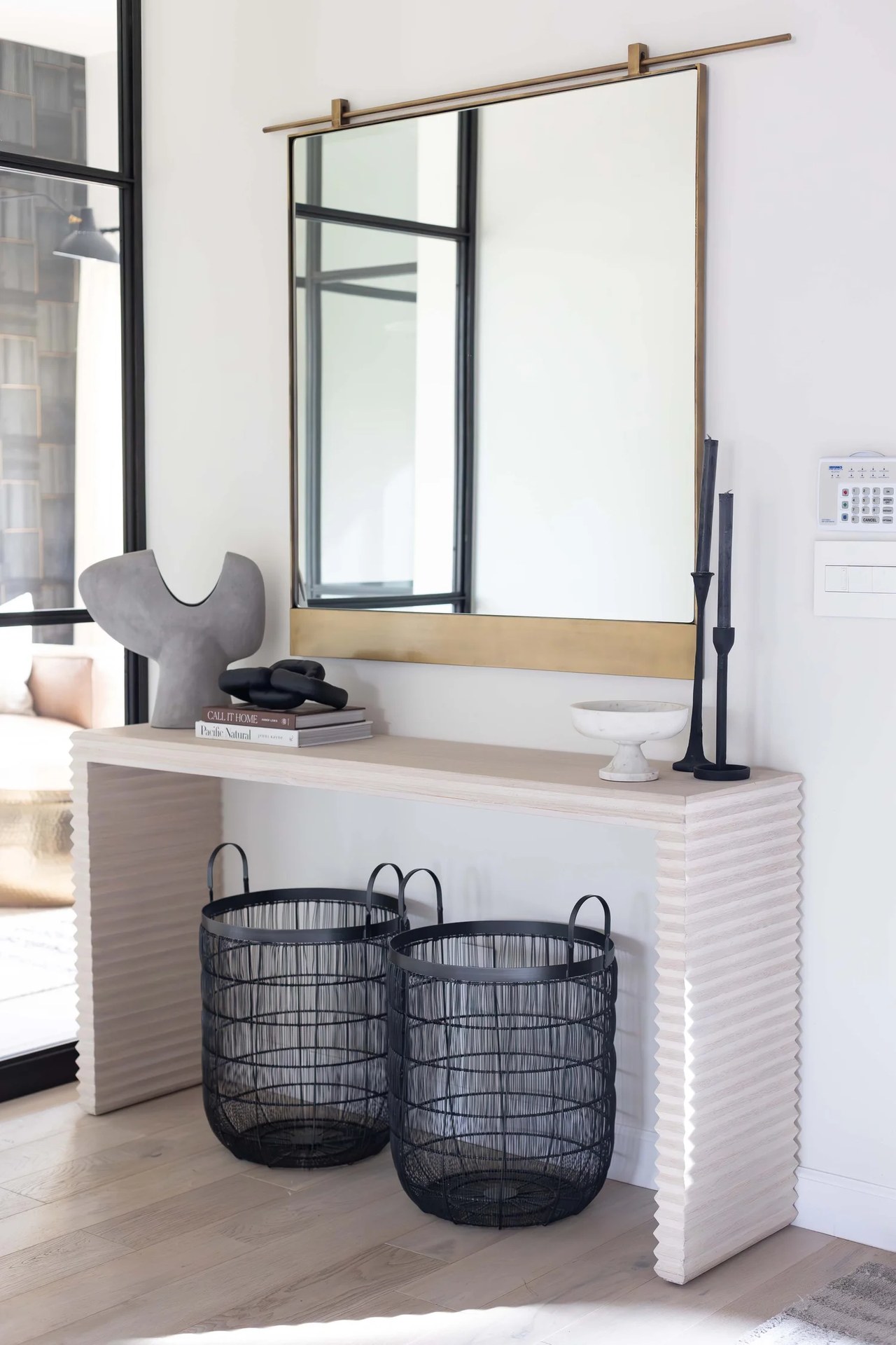 A ribbed stone console, a brass-framed mirror, and two black wire baskets. Devotion, Ancala, Desert Dwelling.