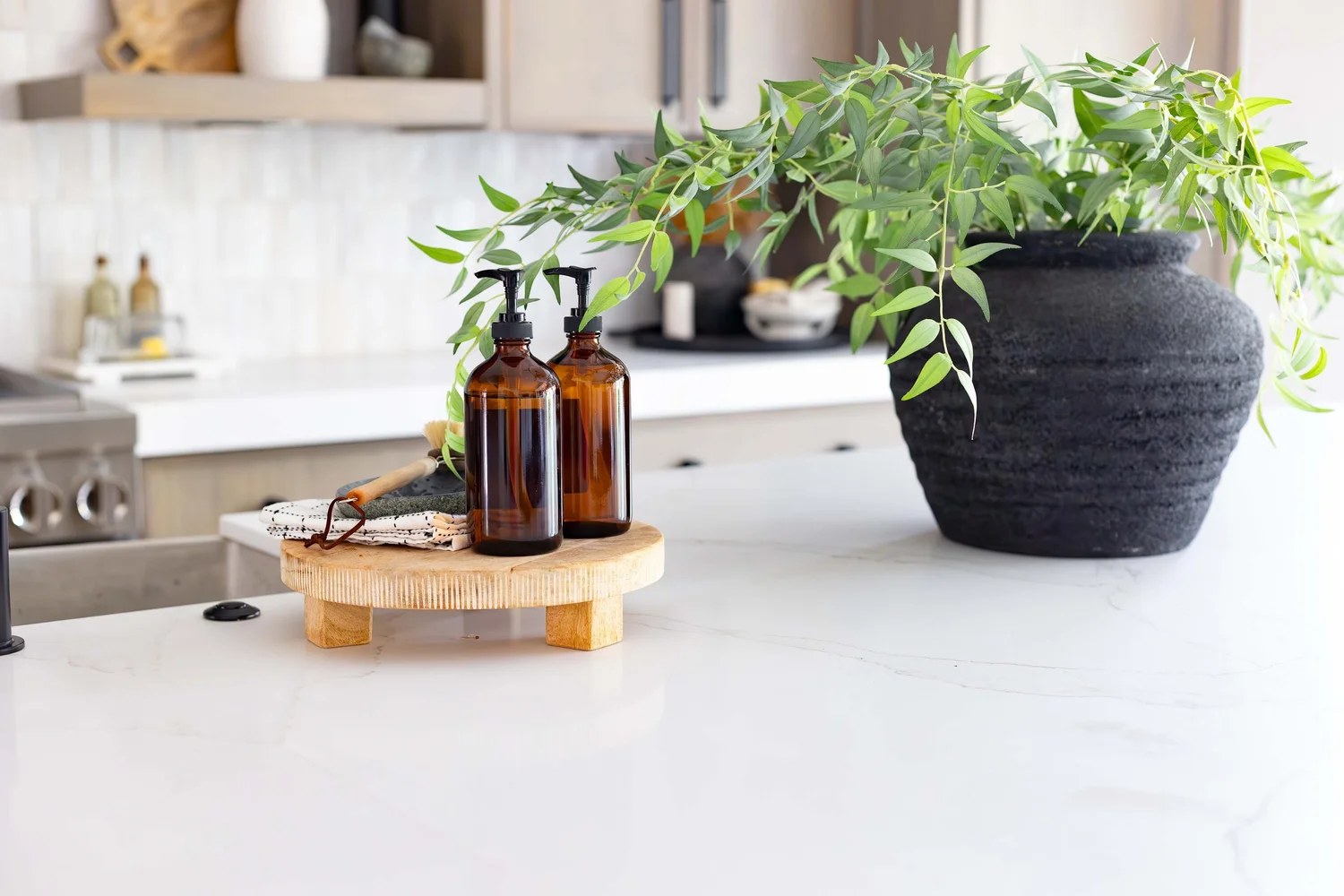 Amber bottles on a low oak stand, eucalyptus in a black vessel, and a white stone island. Devotion, Ancala, Desert Dwelling.