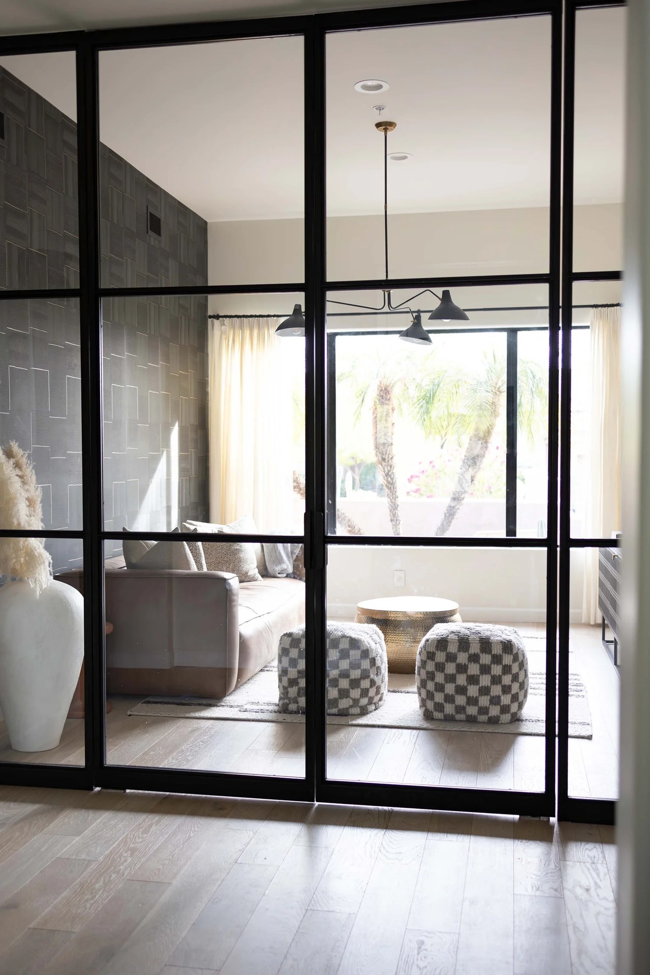 A steel-and-glass partition opening to a lounge of leather, check poufs, and palms. Devotion, Ancala, Desert Dwelling.