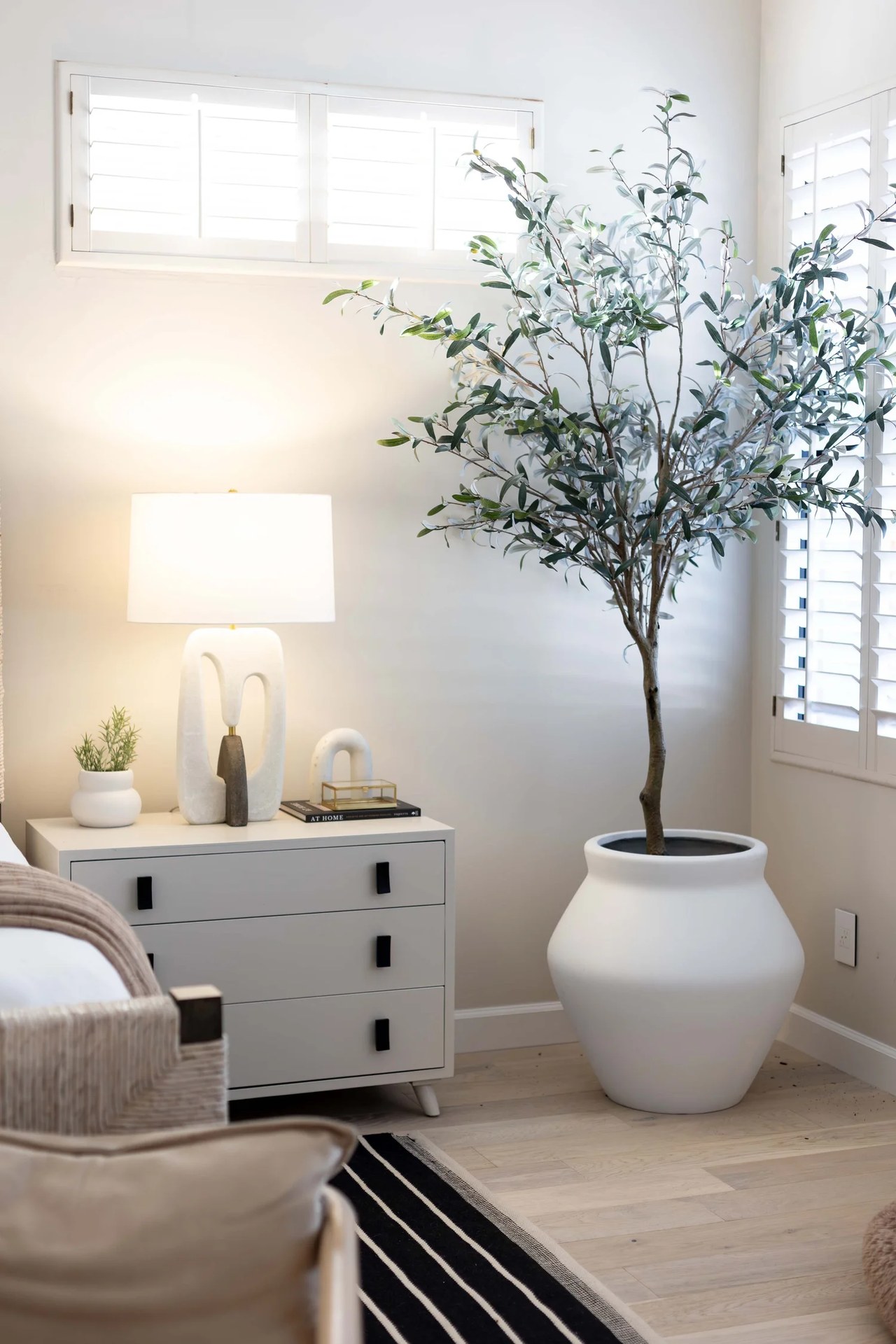 A bedroom corner — a sculptural lamp, a white dresser, and an olive in a clay pot. Devotion, Ancala, Desert Dwelling.