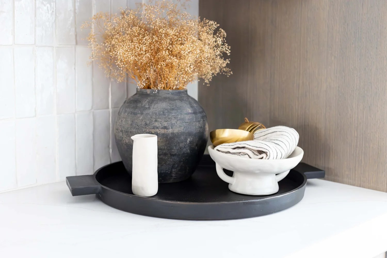 A black tray with a dark vessel of dried blooms, a white pitcher, and folded linen. Devotion, Ancala, Desert Dwelling.
