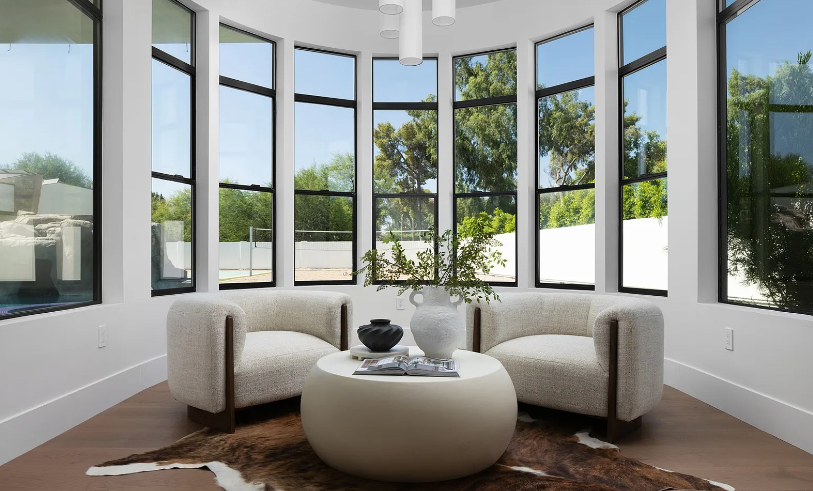 A bay of black-framed windows, two lounge chairs, and a round table to the garden. I, Run, Paradise Valley, Desert Dwelling.