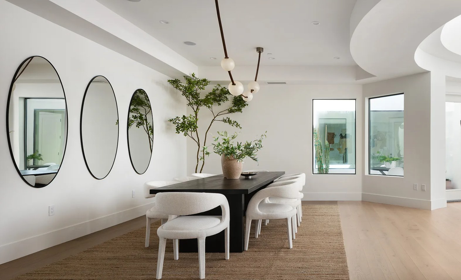 Dining with a dark table, white chairs, and three oval mirrors on a white wall. I, Run, Paradise Valley, Desert Dwelling.