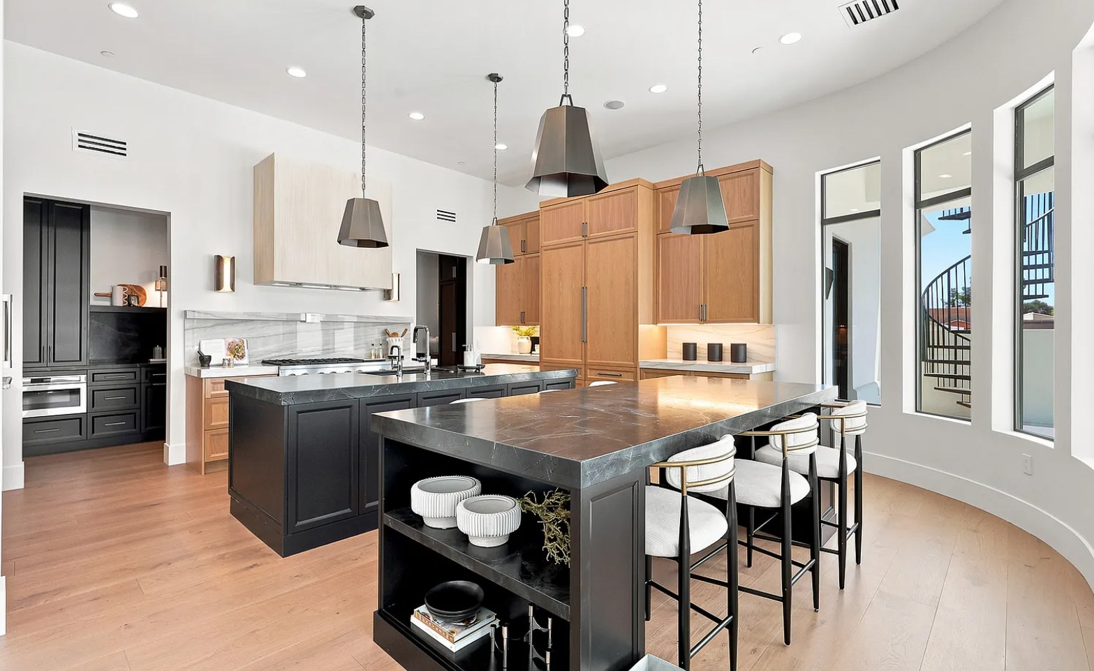 The kitchen at I, Run — black marble islands, oak millwork, and tall windows to a spiral stair. Paradise Valley, Desert Dwelling.