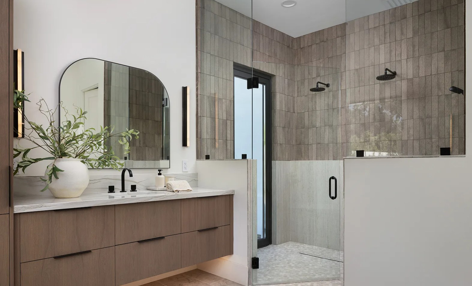 Primary bath — oak vanity, an arched mirror, and a stone shower with a garden window. I, Run, Paradise Valley, Desert Dwelling.