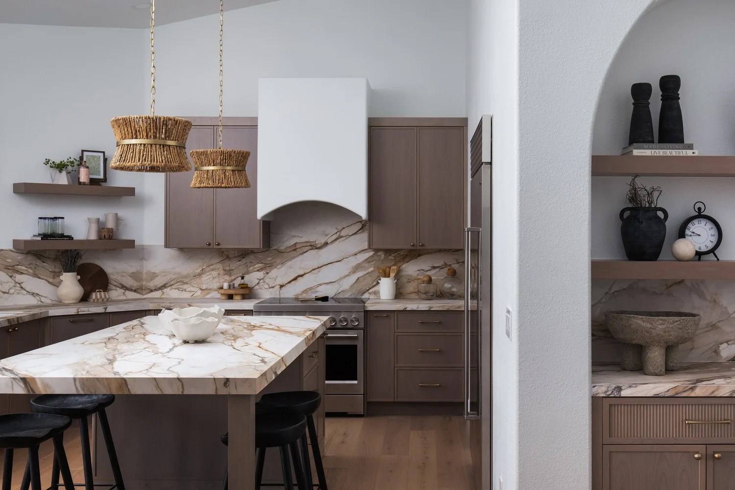 The kitchen from the living room — island, stools, and the arched millwork beyond. New Beginnings, Scottsdale, Desert Dwelling.