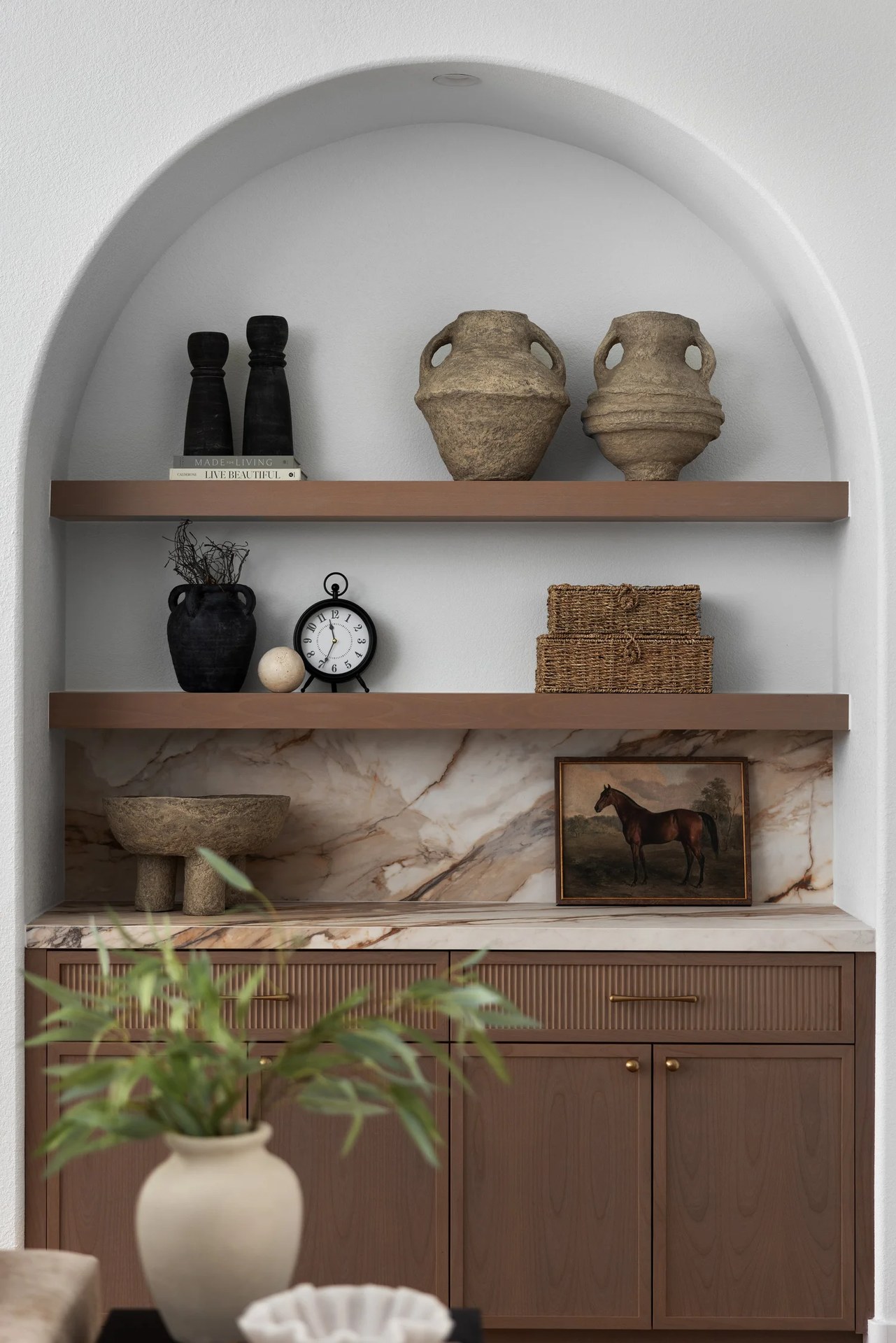 The arched niche in close — clay vessels, a clock, woven boxes, and marble. New Beginnings, Scottsdale, Desert Dwelling.