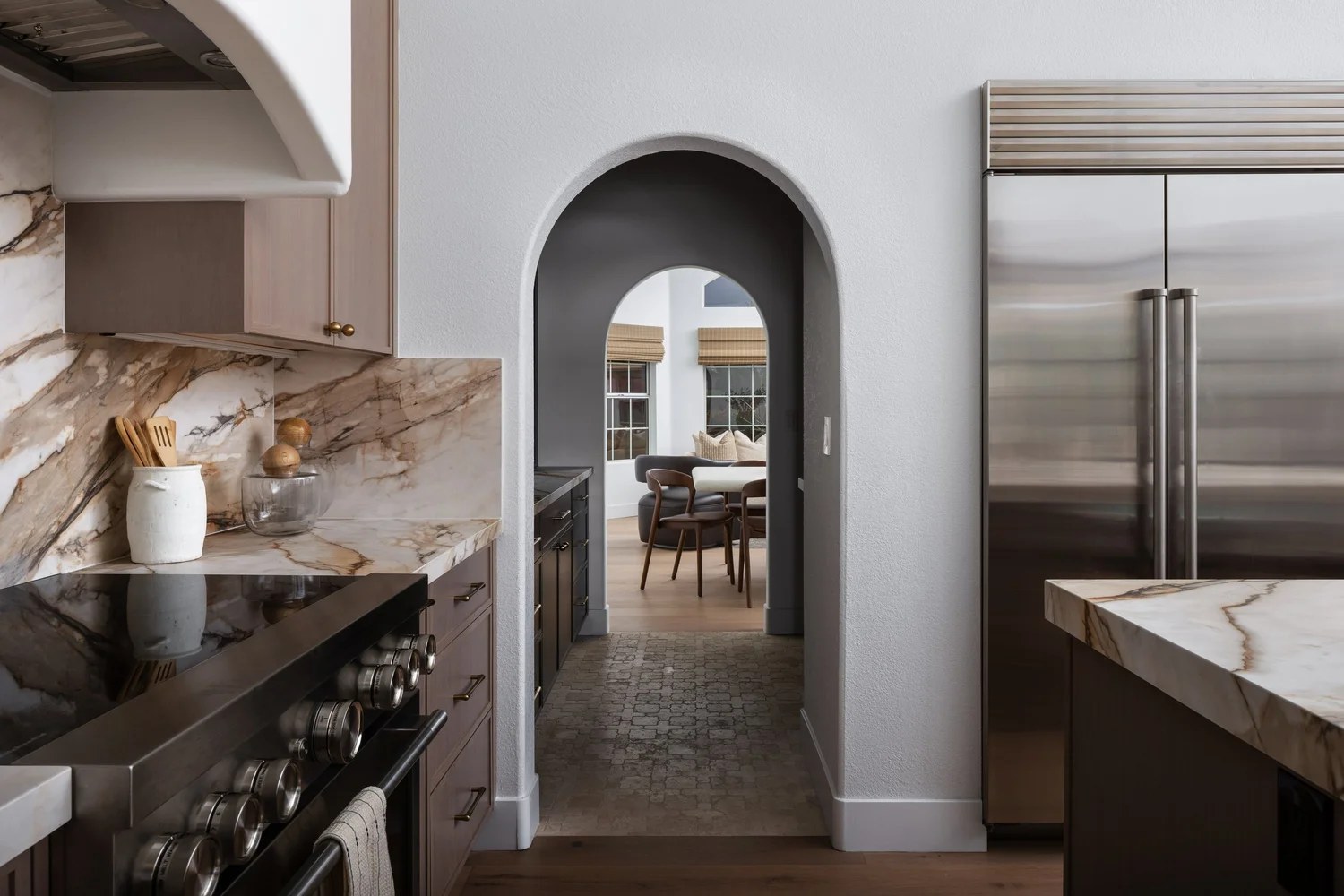 An arched passage from the kitchen to dining, with a steel refrigerator and dark millwork. New Beginnings, Scottsdale, Desert Dwelling.