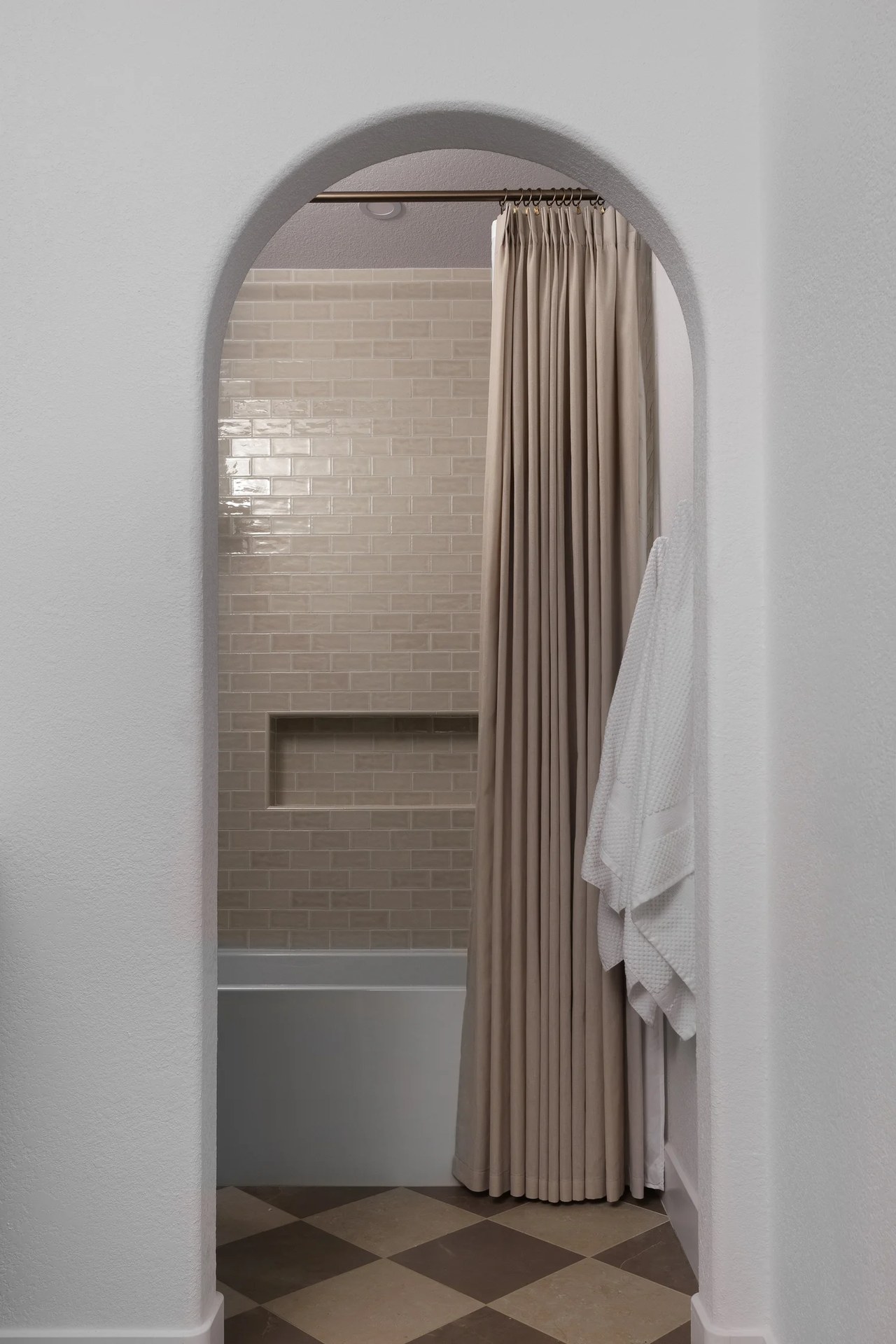 An arched opening to a tiled bath, a gathered linen curtain, and a hanging robe. New Beginnings, Scottsdale, Desert Dwelling.