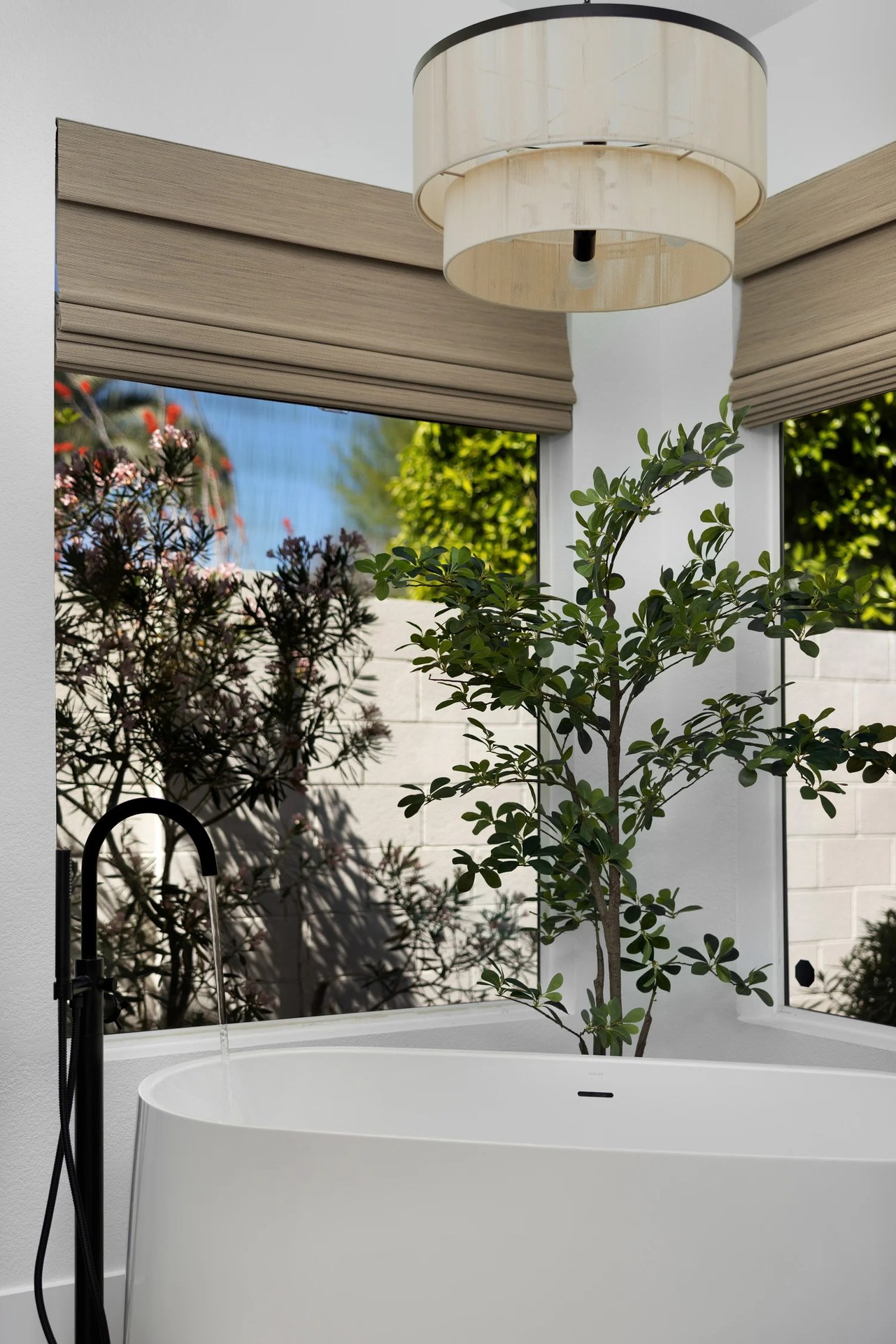A free-standing tub by a corner of garden windows, with a black filler and a small tree. New Beginnings, Scottsdale, Desert Dwelling.