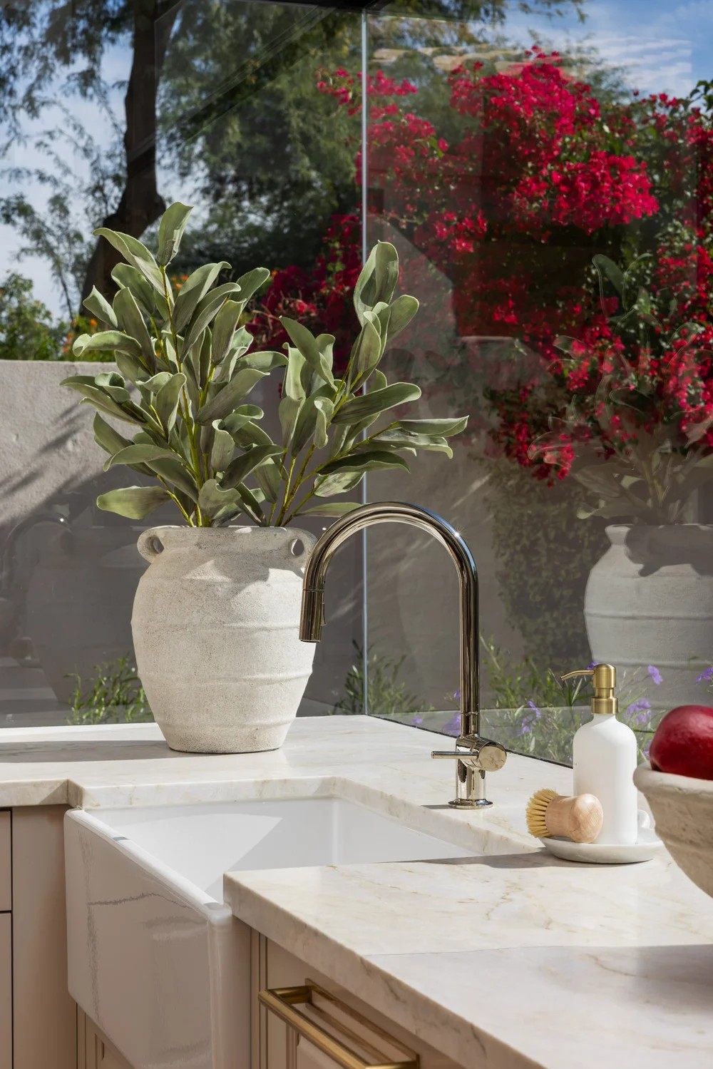 A farmhouse sink and nickel faucet against marble, with bougainvillea through the glass. Tuckey, Scottsdale, Desert Dwelling.